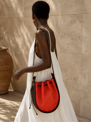 Black female model wearing a white dress with a handmade orange and brown genuine leather round shoulder bag by NUA Bags.