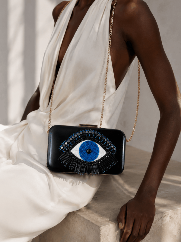 Black female model wearing a white dress with a handmade black hand-embroidered portfolio clutch bag by NUA Bags.