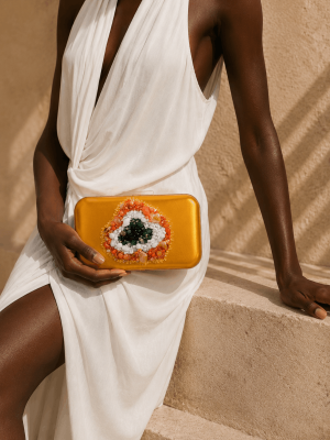 Black female model wearing a white dress holding a handmade mustard yellow embroidered portfolio clutch by NUA Bags.
