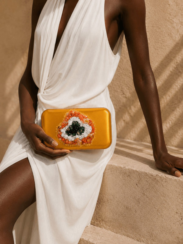 Black female model wearing a white dress holding a handmade mustard yellow embroidered portfolio clutch by NUA Bags.