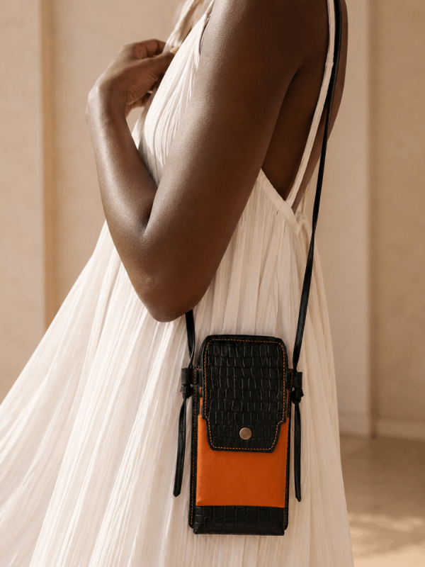 Black female model wearing a white dress with a handmade genuine leather mini crossbody phone bag in black and orange by NUA Bags.