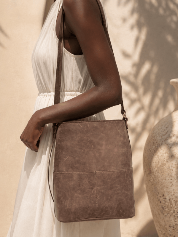 Black female model wearing a white dress with a handmade brown genuine leather boho shoulder bag by NUA Bags.